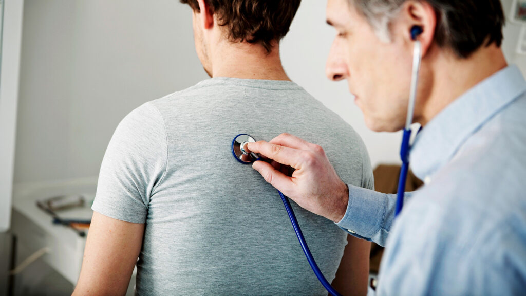 Médecin auscultant le dos d'un patient avec un stéthoscope.