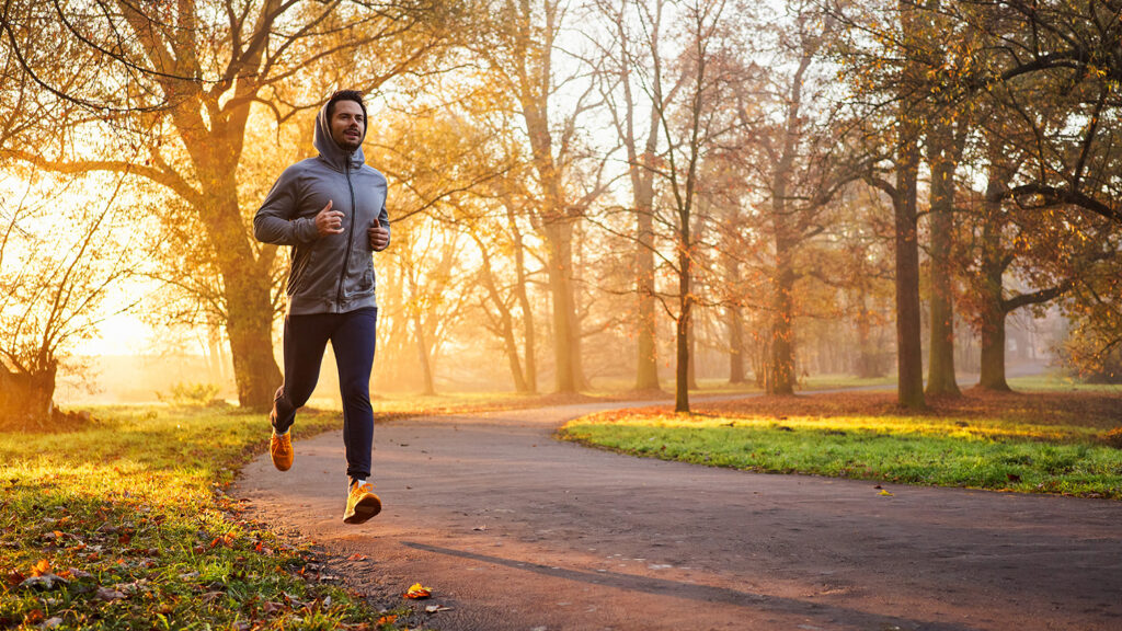 Homme courant sur un chemin forestier parmi les feuilles d'automne.