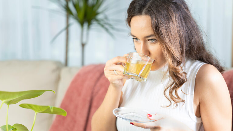 Femme buvant une tisane claire dans un intérieur lumineux.