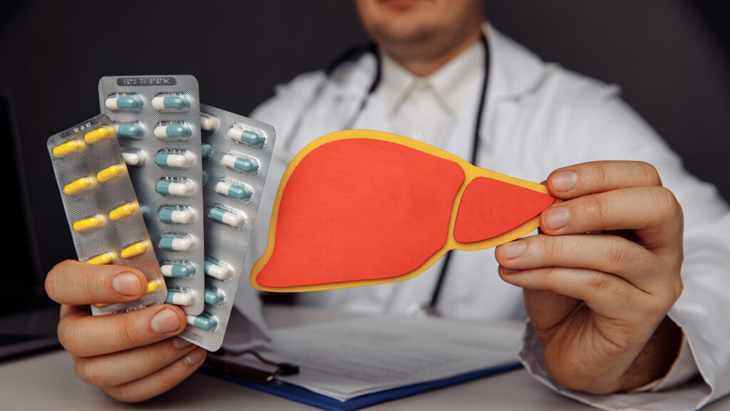 Un médecin tenant des médicaments et une maquette de foie, pointant sur les risques de toxicité hépatique.