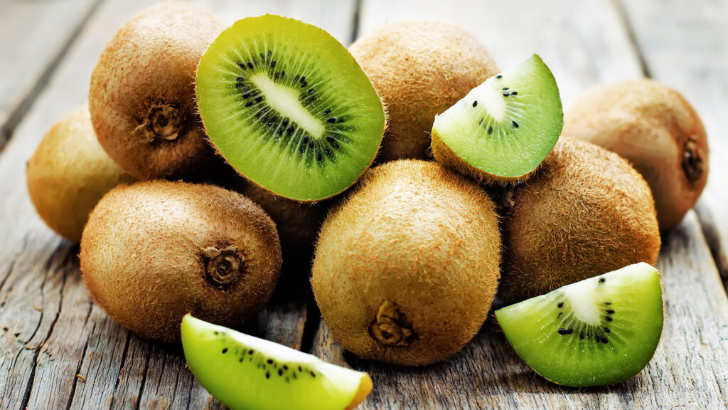 Plusieurs kiwis entiers et tranchés disposés sur une surface en bois rustique.