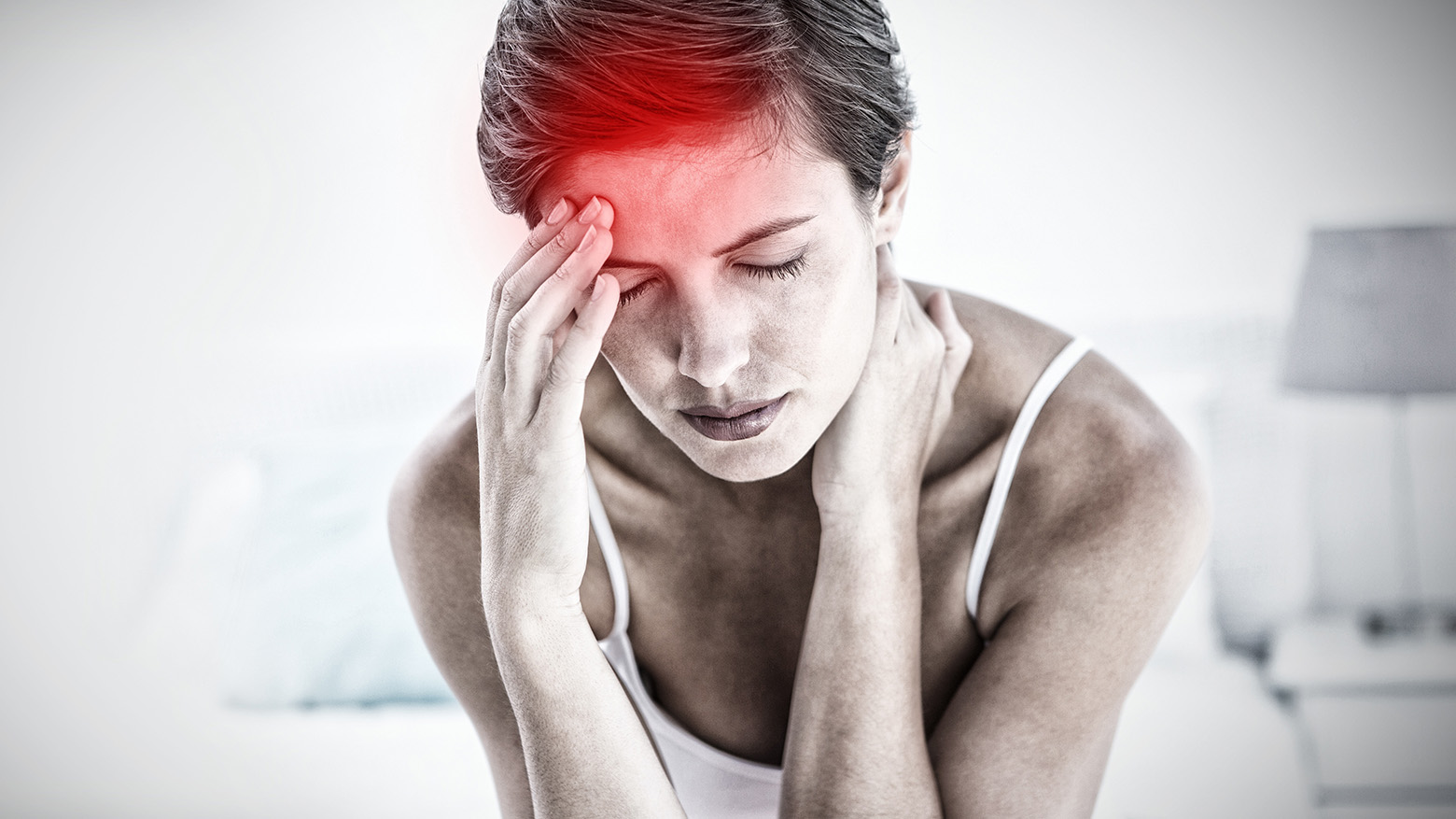 Femme souffrant de migraine aiguë, tenant sa tête avec une zone rouge visible sur son front.