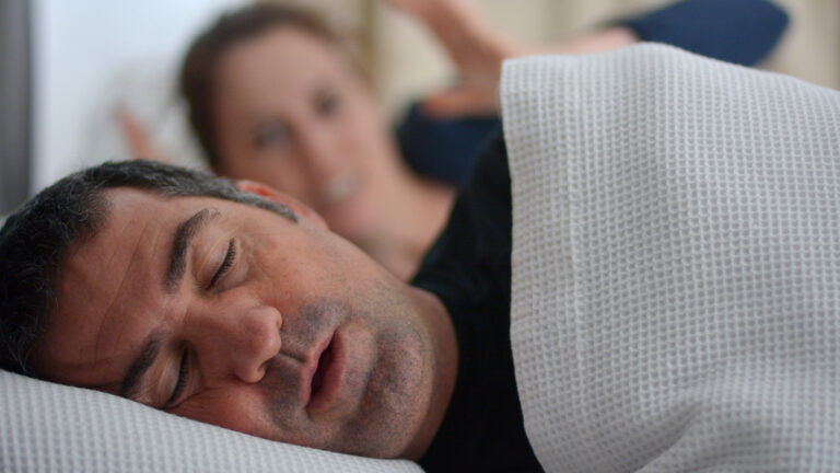 Homme souffrant d’apnée du sommeil avec une femme réveillée en arrière-plan