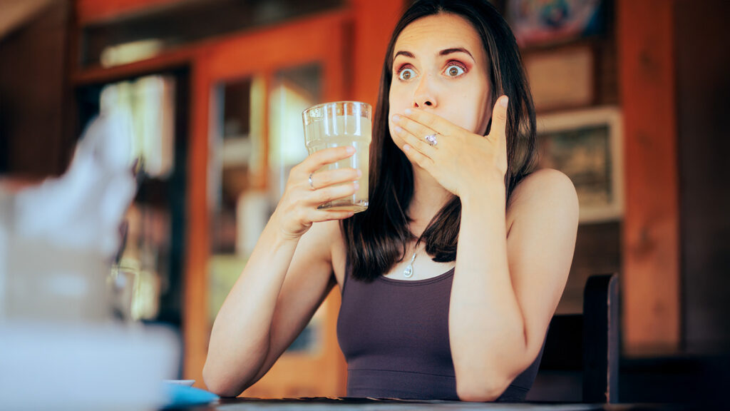 Femme surprise tenant un verre d’eau après avoir eu un hoquet.