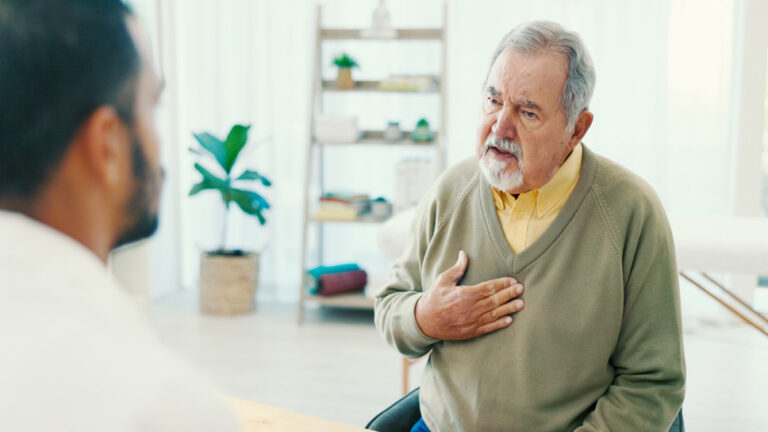 Senior en consultation médicale, posant une main sur sa poitrine, parlant avec un médecin.