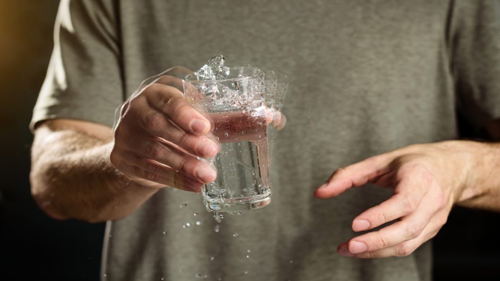 Main d'un homme tenant un verre d'eau, illustrant une main tremblante.