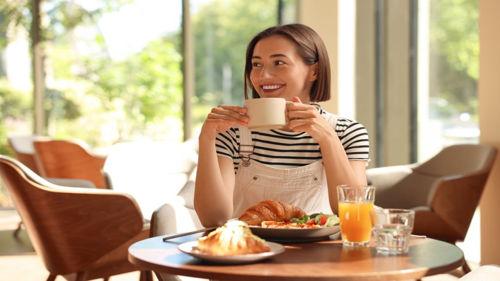 Femme souriante dégustant un petit-déjeuner dans un café.