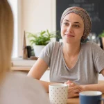 Une femme portant un foulard assise à une table, souriant à une autre personne.
