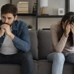 Un homme et une femme assis sur un canapé, l'air préoccupé, ne se regardant pas.