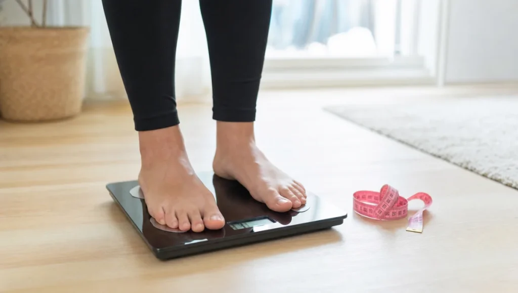 Personne debout sur une balance avec un mètre ruban rose à côté.