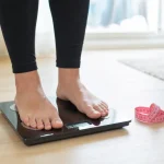 Personne debout sur une balance avec un mètre ruban rose à côté.