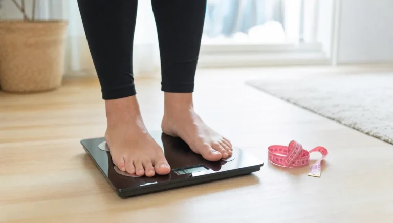 Personne debout sur une balance avec un mètre ruban rose à côté.