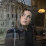 Femme regardant à travers une fenêtre avec un air pensif.