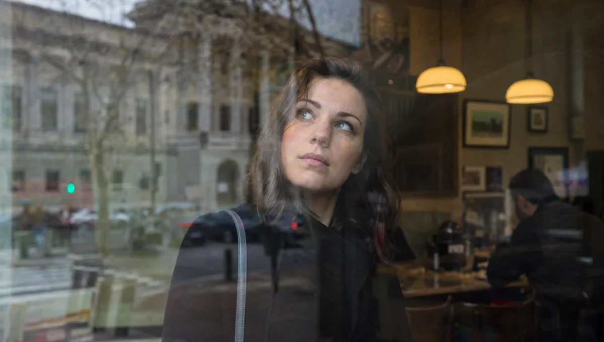 Femme regardant à travers une fenêtre avec un air pensif.